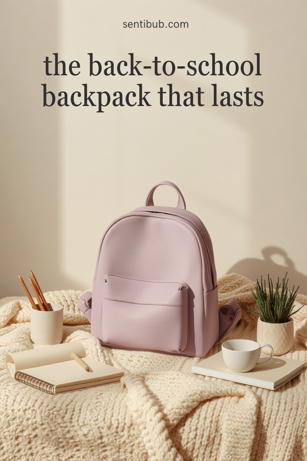 a soft mauve-lilac backpack styled on a cream knit blanket with a spiral notebook, a cup of pens, a mug, and a small potted plant in warm morning light