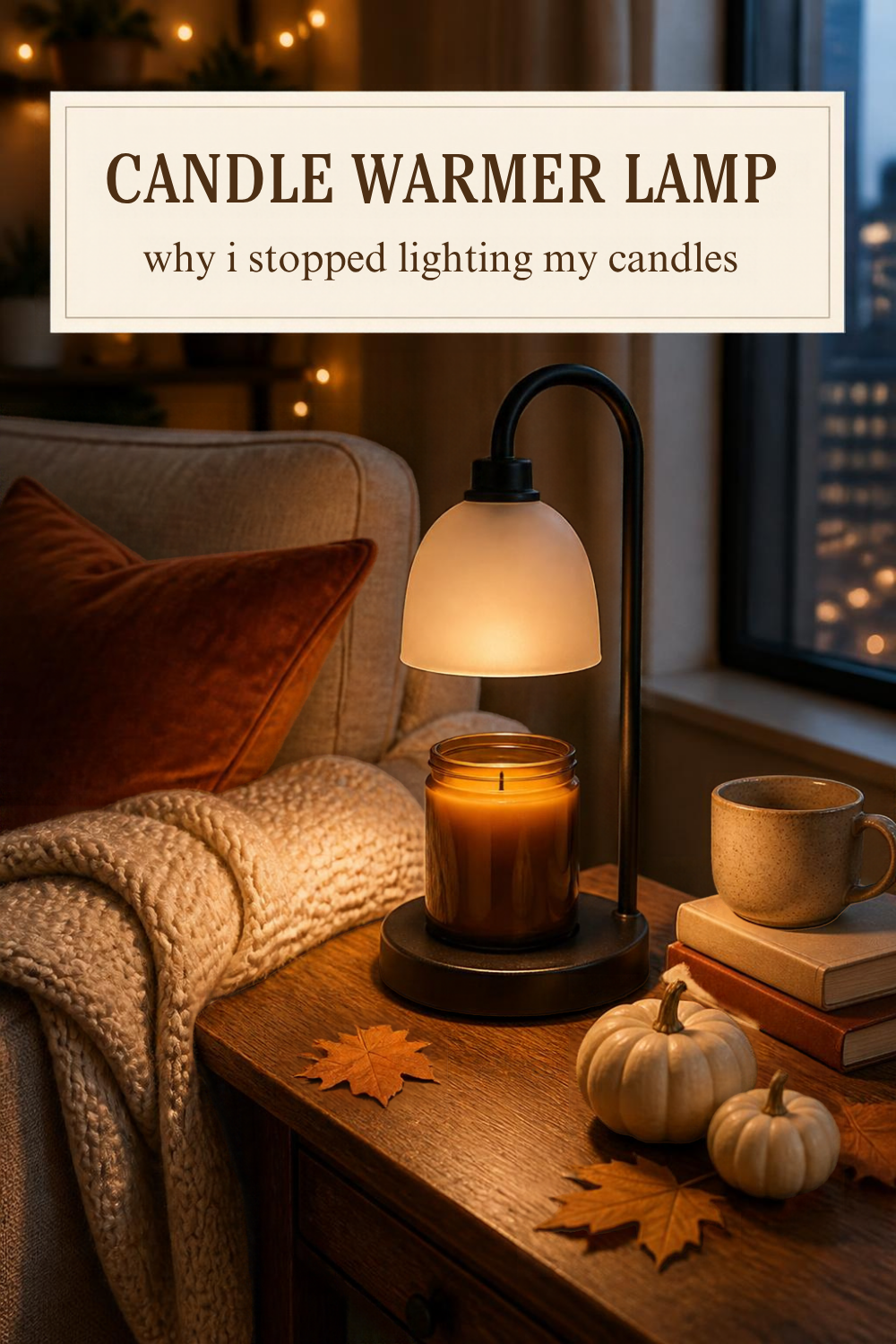 a candle warmer lamp with a black metal base and a frosted glass dome shade glowing over an unlit amber jar candle on a wood side table, next to a cream knit throw on the couch arm, two small white pumpkins, fall leaves, books and a mug