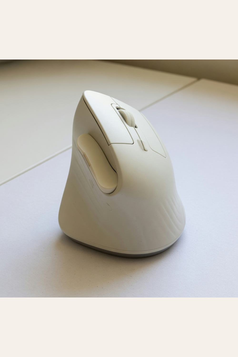off-white vertical ergonomic mouse on a light wood desk beside a keyboard